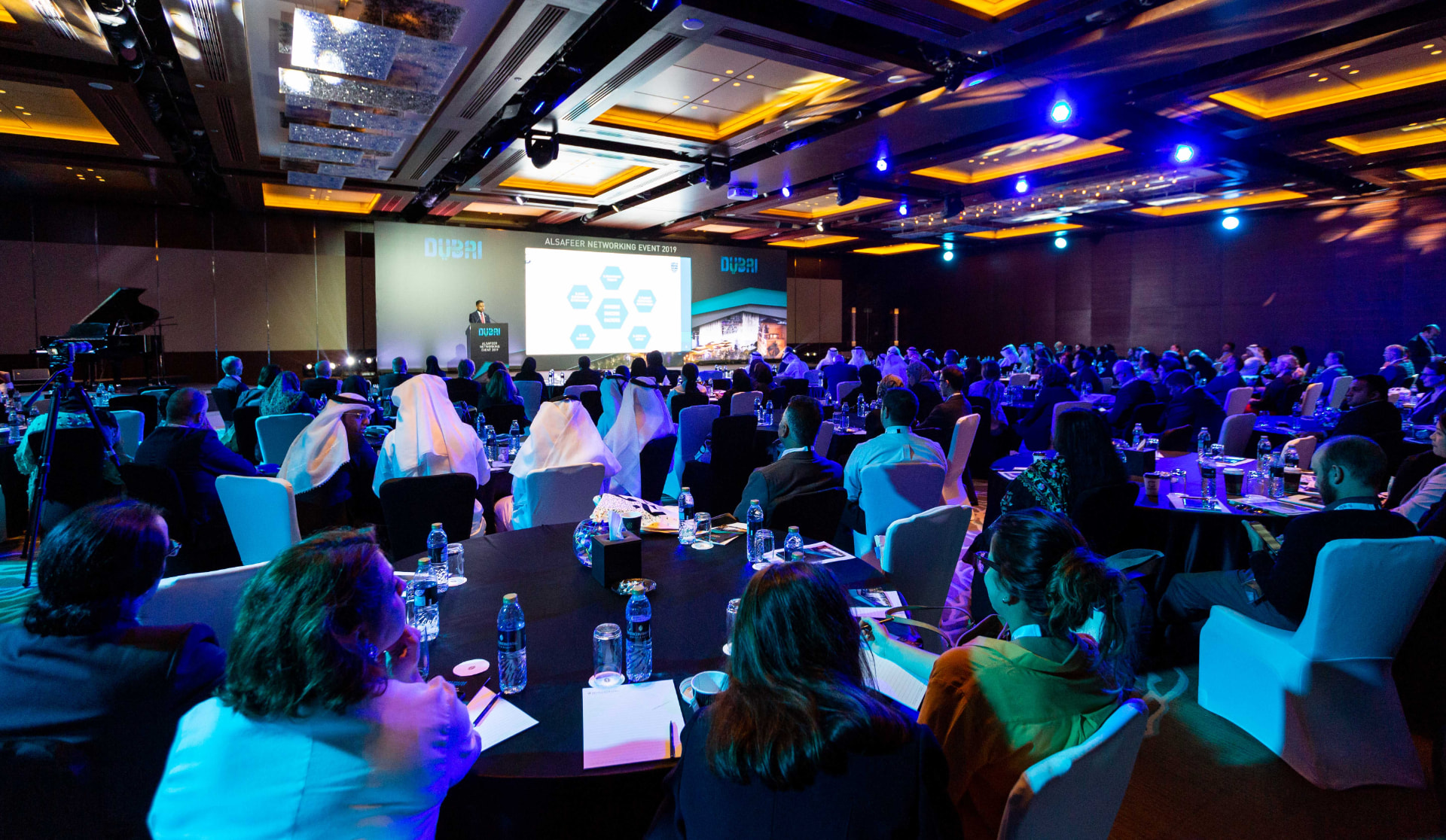Large business networking event with a speaker on stage and a full room of seated guests
